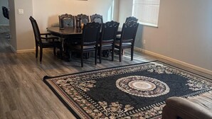A dining area with a table and chairs, a ceiling fan, a chandelier, and a patterned rug.