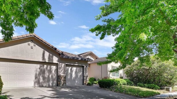 A residential house with a garage, driveway, and surrounding greenery.