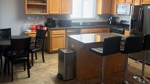 A modern kitchen with wooden cabinets, a central island, bar stools, and a dining area with a table and chairs.