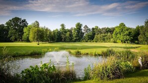 Un parcours de golf avec un étang, des arbres et un ciel dégagé.
