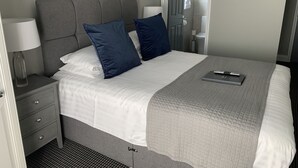 Un lit bien fait, avec une tête de lit grise, deux oreillers, une lampe de chevet et un ordinateur portable posé sur le lit.