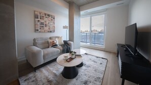 Una sala moderna con un sofá, una mesa de centro, televisor y un ventanal con vistas.