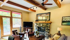 Un salon avec une cheminée en pierre, un téléviseur et un ventilateur de plafond.