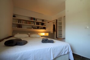 Ein ordentlich bezogenes Bett mit Handtüchern, einer Nachttischlampe und einem Bücherregal mit Büchern.