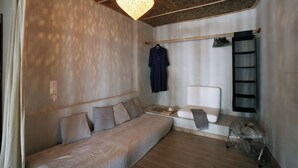 Ein Zimmer mit Bett, Sitzecke, Kleiderstange und Ventilator.