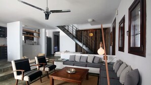 Ein modernes Wohnzimmer mit einer Couch, Sesseln, einem Couchtisch, einem Deckenventilator und einer Treppe, die in eine weitere Ebene führt.