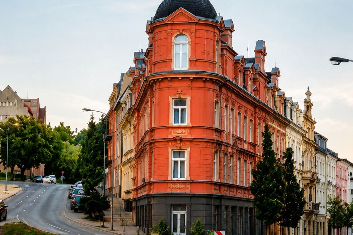 A red building with a dome and a corner entrance, surrounded by trees and other buildings.