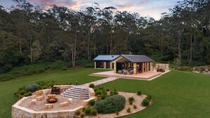 Una casa moderna con un patio, un hogar a leña y una chimenea de piedra rodeada de un jardín ajardinado.