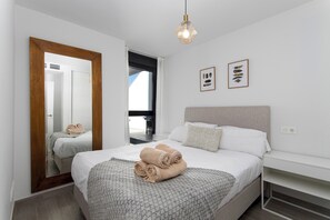 Ein modernes Hotelzimmer mit einem großen Bett, einem Nachttisch, einem Spiegel und Blick ins Freie.
