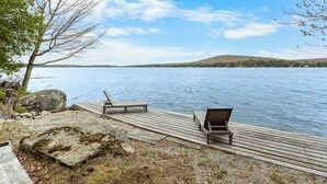 Un molo in legno con panchine che si affaccia su un lago tranquillo, circondato da alberi e una collina in lontananza.