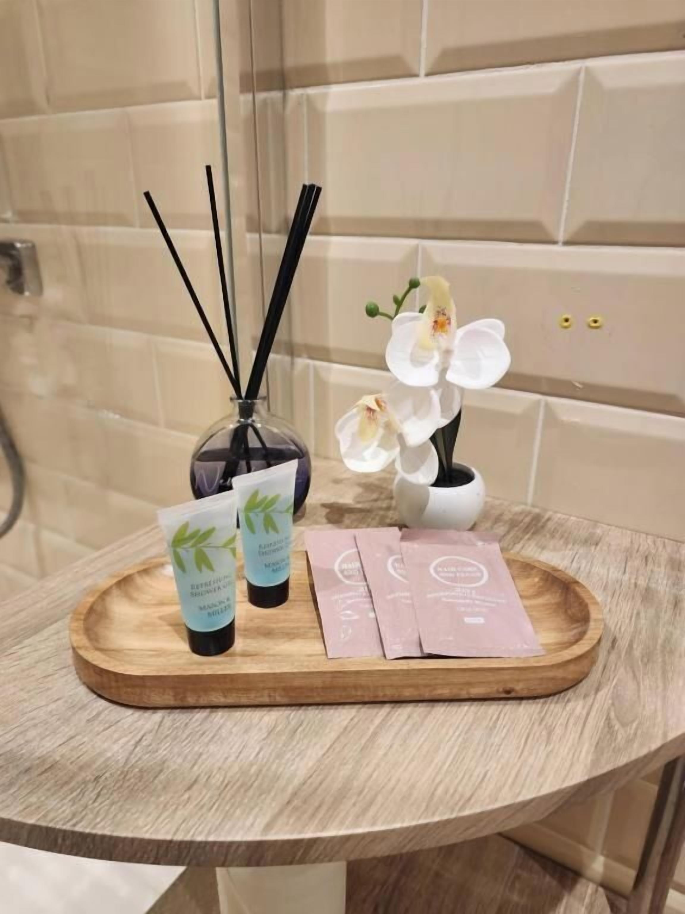 Ein Badezimmer-Waschtisch mit einer Holztasche, die eine Handseifenflasche, eine Lotiontube und eine kleine Vase mit weißen Blumen enthält.