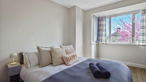 A bedroom with a bed, pillows, a bedside lamp, and a window with curtains. - Bright 3-Bed House in Watford Near London Links & Studios (Hertfordshire)