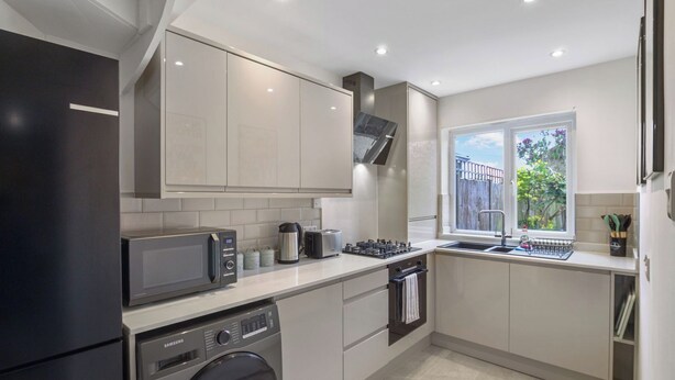 A modern kitchen with a washing machine, microwave, toaster, and sink. - Bright 3-Bed House in Watford Near London Links & Studios (Hertfordshire)