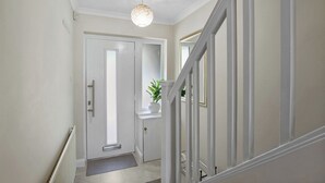 A hallway with a white door, a potted plant, and a staircase with white railings. - Bright 3-Bed House in Watford Near London Links & Studios (Hertfordshire)