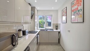 A modern kitchen with a built-in oven, a gas stove, and a window with a view of greenery. - Bright 3-Bed House in Watford Near London Links & Studios (Hertfordshire)