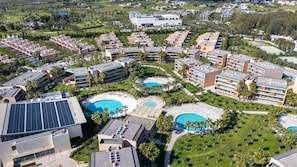 Ein Resort mit mehreren Schwimmbecken, einem Gebäude mit Solaranlage und einem Golfplatz im Hintergrund.