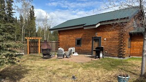 Une cabane en rondins dotée d’un patio, d’un espace salon extérieur et d’un barbecue.