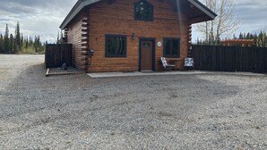 Une cabane en rondins avec une cheminée, une porte et deux fenêtres.