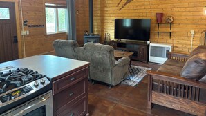 Un intérieur de chalet chaleureux, avec un revêtement en bois, une cheminée, un téléviseur et un coin repas.