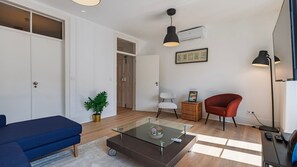 Un salon moderne avec une table basse en verre, un canapé bleu, un fauteuil rouge et une petite table d’appoint sur laquelle est posée une plante.