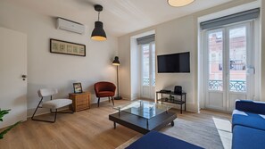 A modern living room with a glass coffee table, a red armchair, a floor lamp, and a flat-screen TV mounted on the wall. - Classy 3-Bedroom Lisbon Apartment by LovelyStay (Lisboa)