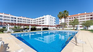 Ein Swimmingpool mit klarem, blauem Wasser, umgeben von Liegestühlen und Sonnenschirmen, mit mehrstöckigen Gebäuden im Hintergrund.
