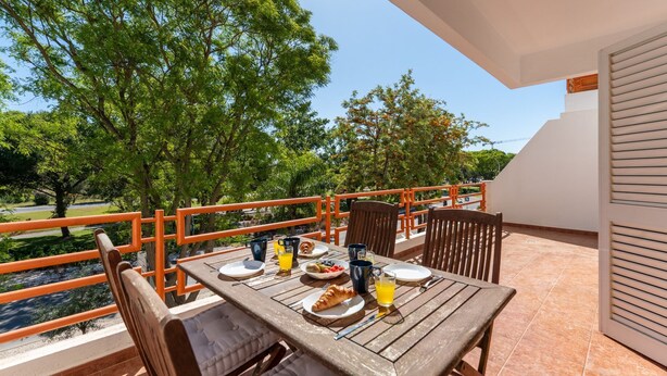 Ein Balkon mit Frühstückstisch, Sitzgelegenheiten im Freien und Blick auf Bäume und eine Straße.
