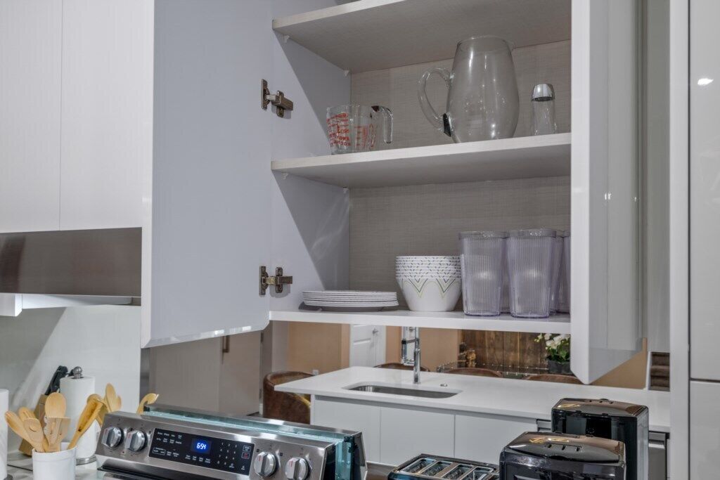 Eine moderne Küche mit weißen Schränken, einer Edelstahl-Dunstabzugshaube, einem Einbauofen, einem Spülbecken und einer Arbeitsplatte mit Toaster und Wasserkocher.