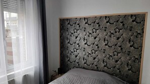 A bedroom with a bed, a window with blinds, and a patterned headboard. - Le Saint Jacques (Douai)