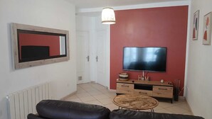 A living room with a black leather sofa, a wooden coffee table, a TV on a red wall, and a white door. - Le Saint Jacques (Douai)