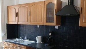 A kitchen with wooden cabinets, a black countertop, a coffee maker, and a stove. - Le Saint Jacques (Douai)