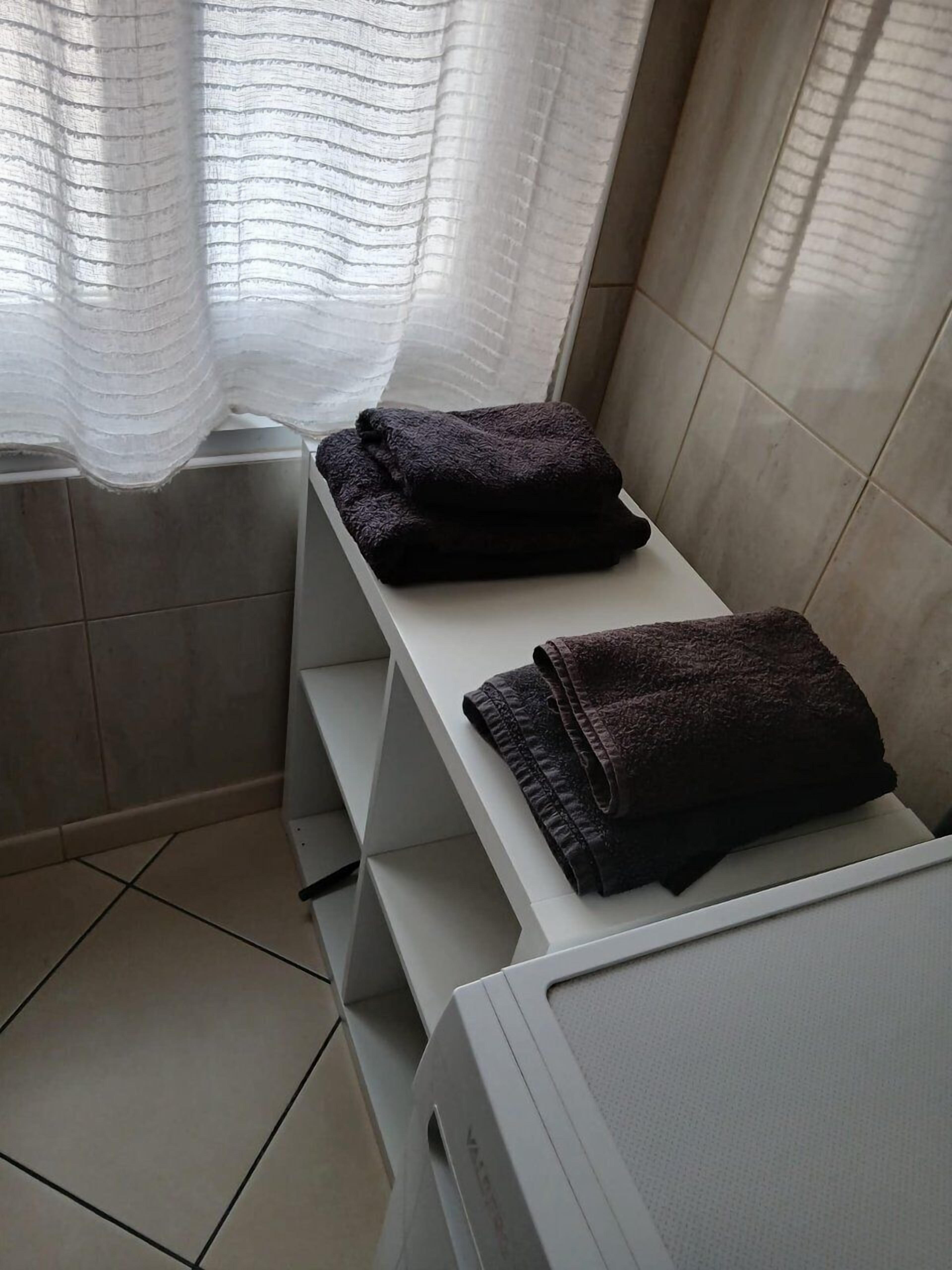 Ein Badezimmer mit einem weißen Waschbecken, einem Spiegel und zwei gefalteten Handtüchern auf einem Regal.
