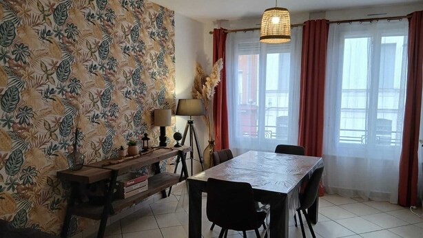 A dining area with a table and chairs, a lamp, a bookshelf, and a window with curtains. - Le Saint Jacques (Douai)