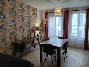 A dining area with a table and chairs, a lamp, a bookshelf, and a window with curtains. - Le Saint Jacques (Douai)