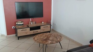 A living room with a flat-screen TV, a wooden cabinet, a round coffee table, and a black leather sofa. - Le Saint Jacques (Douai)
