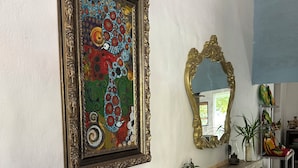 En hall med ett inramat konstverk, en spegel, en lampa och en hylla med diverse föremål.