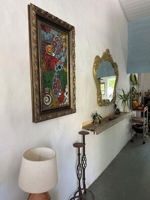 Ein Flur mit einem gerahmten Kunstwerk, einem Spiegel, einer Lampe und einem Regal mit diversen Gegenständen.
