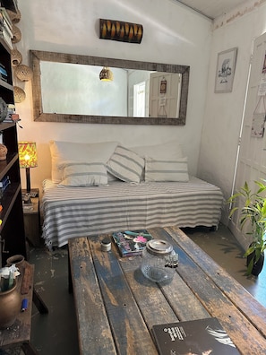 Ein gemütliches Zimmer mit einem Bett, einem Holztisch, einem Bücherregal, einer Lampe und einem Spiegel.