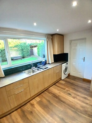 A compact kitchen with a built-in washing machine, a large window, and a view of the garden. - House near moors, 10 minutes walk to high street (Guisborough)