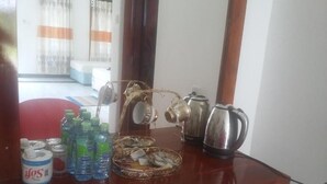 Una encimera de madera con una cafetera, un hervidor y un plato con aperitivos. Hay botellas de agua y una lata de jugo.