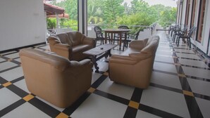 Un espacio de estar al aire libre cubierto, con sofás de cuero y una mesa, suelo de cuadros y vistas a zonas verdes.