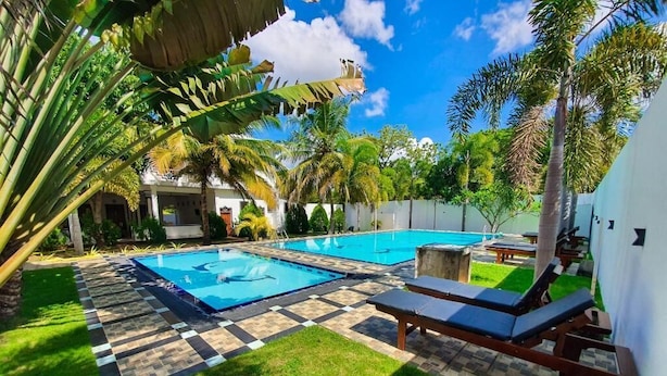 Una piscina con dos sillones de descanso, rodeada de palmeras y un suelo con estampado de cuadros.