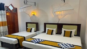 Habitación de hotel con dos camas, cada una con colcha amarilla y ropa de cama blanca, una puerta de madera y una lámpara fijada a la pared.