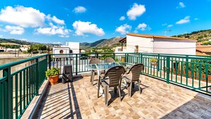 Une terrasse dotée d’une table et de chaises en verre, entourée d’une rambarde verte, et offrant une vue sur un paysage vallonné.