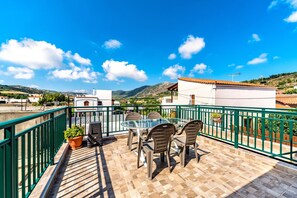Eine Terrasse mit Glastisch und Stühlen, einem Blumentopf und Blick auf die umliegende Landschaft.