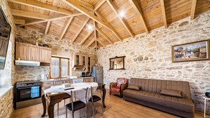 Une cuisine rustique aux murs de pierre, avec des poutres en bois et un coin repas comprenant une table et des chaises.
