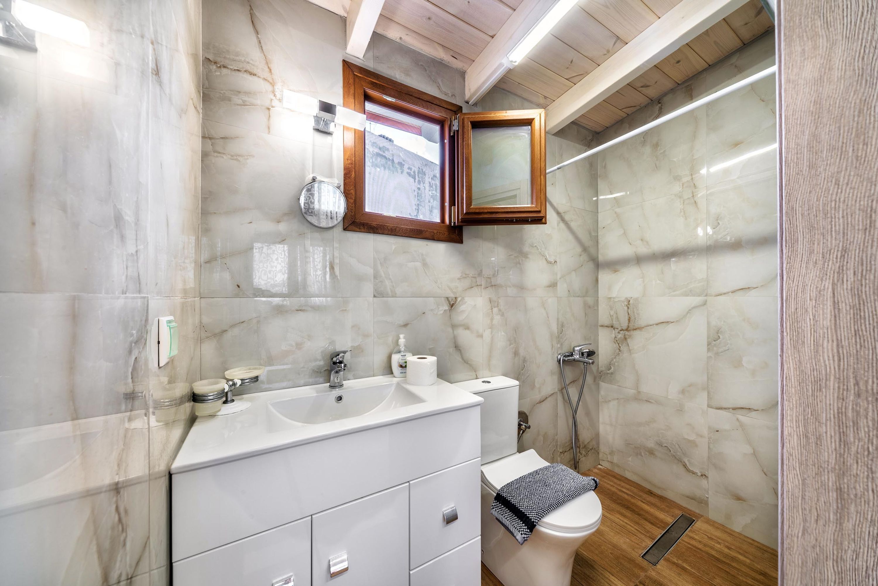 A bathroom with marble walls, a white sink with two basins, a toilet, and a shower area.