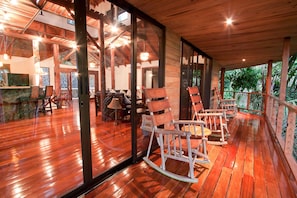 A wooden deck with rocking chairs and a glass wall overlooking a dining area. - Charming 3-bedroom house with AC in beautiful Quepos (Quepos)