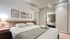 Una habitación de hotel moderna con una cama grande, una mesita de noche con lámpara, un armario y cuadros en la pared.