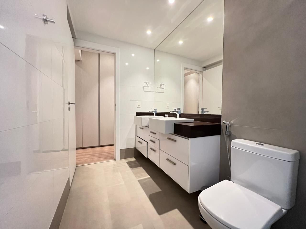 A modern bathroom with a white toilet, a large mirror, and a vanity with a black countertop.